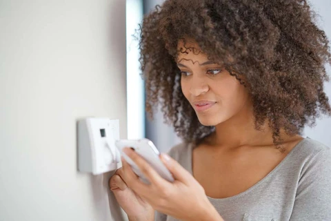 Une femme aux cheveux boucl&eacute;s ajuste un thermostat mural blanc dans un int&eacute;rieur moderne