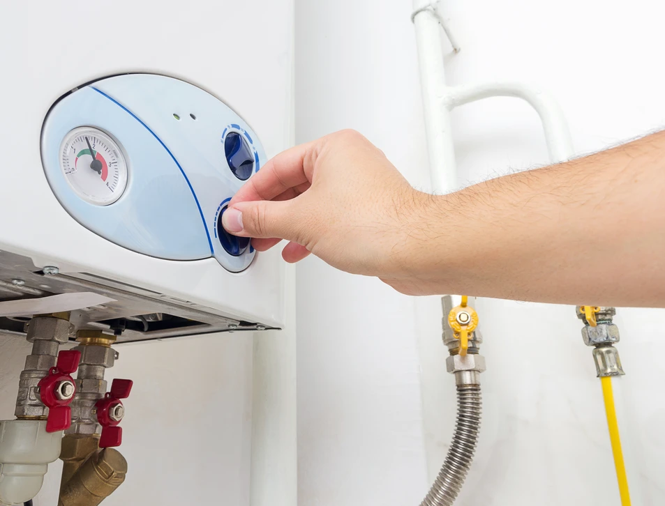 Une main ajuste le thermostat d'une chaudière domestique murale blanche