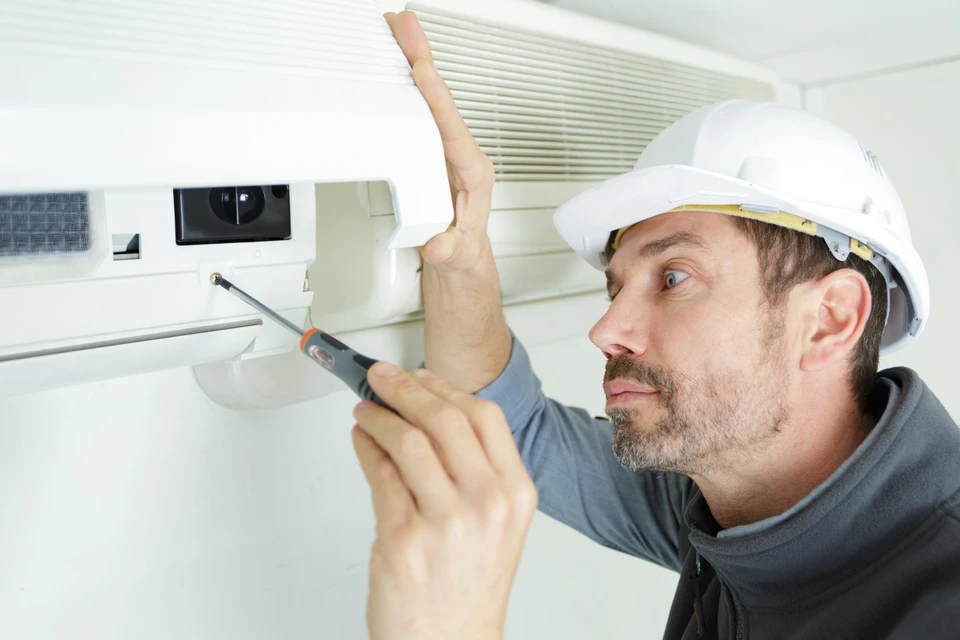 Technicien HVAC en uniforme vert travaillant sur système de chauffage/climatisation dans intérieur résidentiel