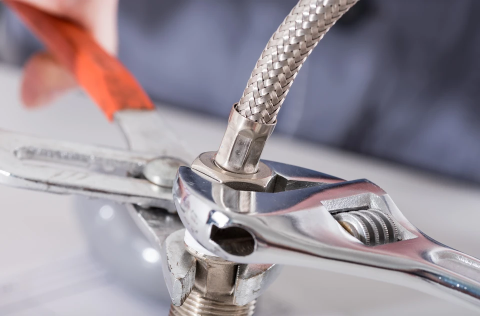Homme souriant en tenue de travail blanche avec ceinture &agrave; outils orange, effectuant un geste d'appel t&eacute;l&eacute;phonique sur fond neutre
